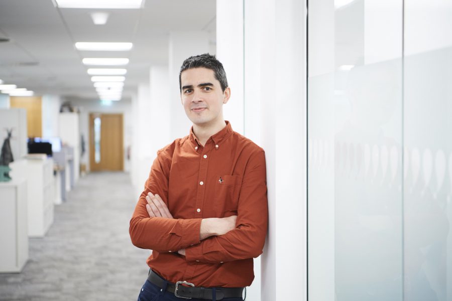 Man smiling and leaning against a white wall in an office environment