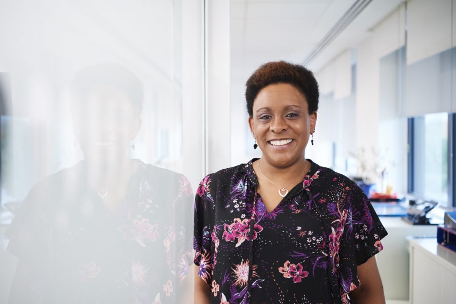 Woman smiling and leaning against a white wall in an office environment